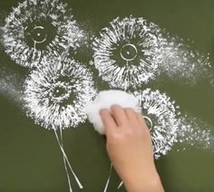 a person is using a sponge to paint dandelions on a blackboard with white chalk