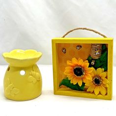 a yellow vase next to a photo frame with sunflowers on it and a beehive