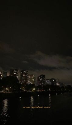 the city is lit up at night with lights reflecting in the water and dark clouds