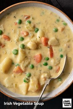 a bowl of soup with peas, potatoes and carrots in it next to a spoon