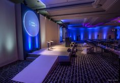 an empty room is lit up with blue lights and white carpeted flooring, along with several tables and chairs