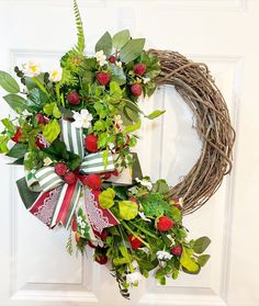 a wreath is hanging on the front door with flowers and greenery around it,