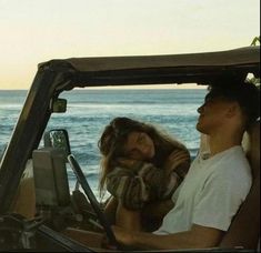 a man and woman sitting in the back of a truck on the beach near the ocean