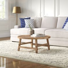 a living room with white couches and blue pillows on the floor, along with a wooden coffee table