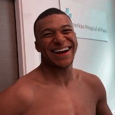 a man with no shirt smiling in front of a hospital sign and holding a toothbrush