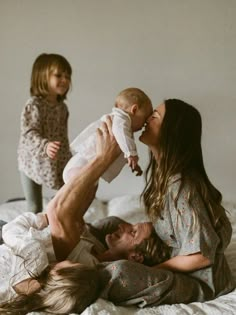 a man laying on top of a bed holding a baby next to two women and a child