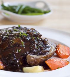 a white plate topped with meat covered in gravy next to green beans and carrots