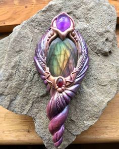 a purple and green brooch sitting on top of a wooden table next to a rock