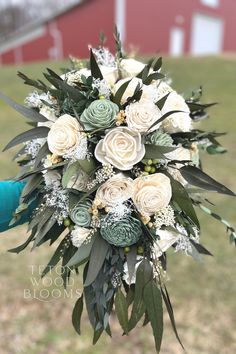 a bridal bouquet with white flowers and greenery in front of a red barn