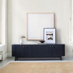 an empty room with a black sideboard and framed pictures on the wall above it