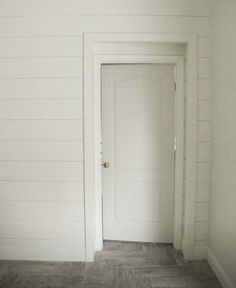 an empty room with a white door and gray tile floor in front of the wall