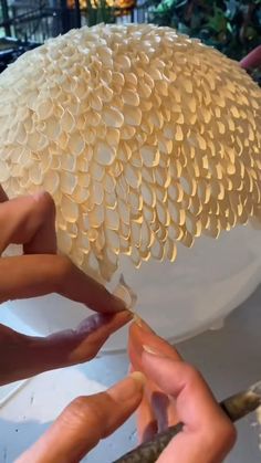 two hands are working on an object that looks like a large white flower with petals