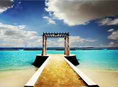 an empty pier on the beach with blue water and white clouds in the sky behind it