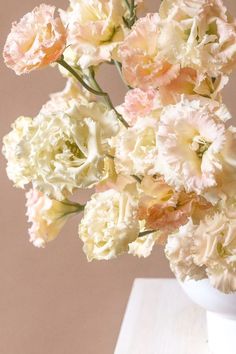 a white vase filled with pink and white flowers on top of a wooden table next to a wall