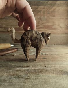 a hand is holding a small toy cat on a wooden table next to other items