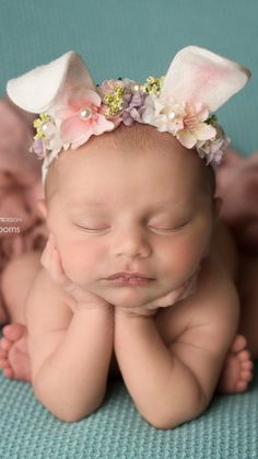 a baby is laying on its back wearing a bunny ears headband with flowers in it's hair