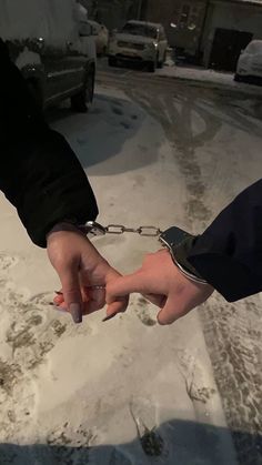 two people holding hands in the middle of a snow covered parking lot with cars behind them