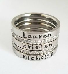 three silver rings with names engraved on the sides and diamonds set in them, all stacked together