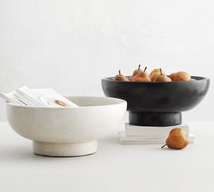 two bowls filled with fruit sitting on top of a white table next to each other