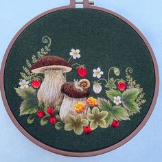 an embroidery kit with two mushrooms and flowers on the front, in a circular frame