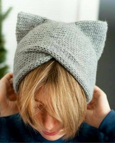 a woman wearing a gray knitted hat with a cat ears on it's head