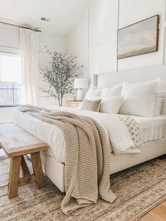 a bedroom with a large bed and white walls in the corner, along with a wooden bench at the foot of the bed