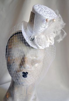 A Mad Hatter fascinator hat with a bridal twist! The hat is covered with beautiful textured ivory brocade and embellished with ivory satin ribbon around the crown. Trimmed with pearl hats pins, ivory roses and hydrangea blossoms,ivory feather spray, the signature 10/6 Mad Hatter card and of course a tiny silver tea-pot! Cause around here it's always tea-time! Both hat pins have push-in clasps to avoid accidents! Veil may be added at an extra cost. This mini top hat is fully lined with satin and White Vintage Fascinator For Royal Ascot, Vintage White Costume Hats And Headpieces For Wedding, Vintage White Wedding Costume Hats And Headpieces, Vintage White Costume Hats For Wedding, White Vintage Wedding Costume Hats And Headpieces, Fitted Cream Costume Hats And Headpieces For Ceremony, Vintage White Hat Headpiece, White Hat For Vintage Events, White Fitted Top Hat With High Crown