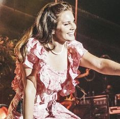 a woman in a pink dress is sitting on a stage with her hand out to the side