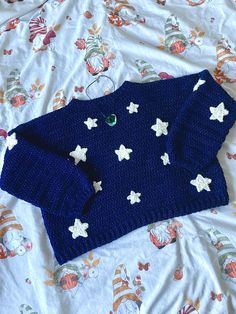 a blue sweater with white stars on it laying on a floral bed sheet, next to a pair of eyeglasses