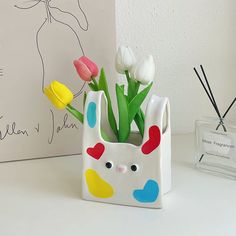 a vase with flowers in it sitting on a table next to a glass block that has an image of a bunny holding tulips