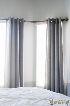 a bed with white sheets and gray curtains