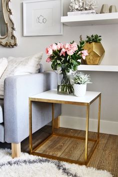 a white table with pink flowers on it and a gold planter next to it