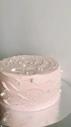 a pink frosted cake sitting on top of a glass table next to a white wall