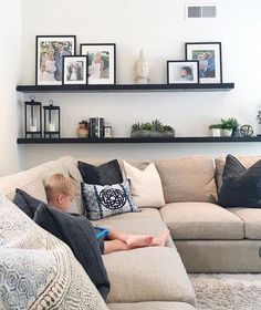 a young boy sitting on top of a couch in front of a wall filled with pictures