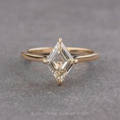 a yellow gold ring with an emerald cut diamond in the center, sitting on a gray surface