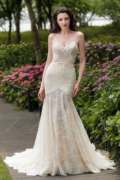 a woman in a wedding dress standing on a path with flowers and bushes behind her