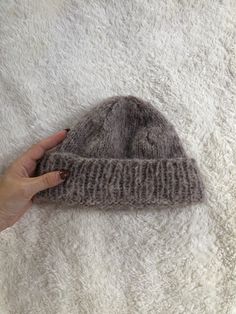 a hand is holding a gray knitted beanie on a white blanket with fuzzy fur