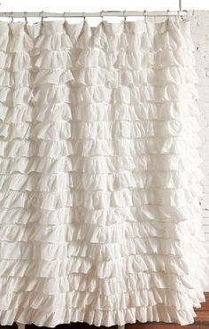 a white shower curtain with ruffles hanging from it's side in front of a brick wall