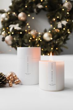 two candles sitting next to each other near a wreath and christmas tree in the background