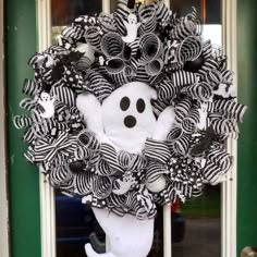 a wreath decorated with black and white striped ribbons, a ghost face on the front door