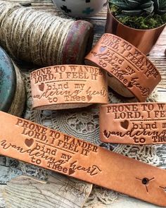 leather bracelets with words and hearts on them sitting next to some thread spools