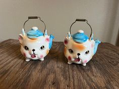 two ceramic teapots with cats painted on them sitting on a wooden table next to each other