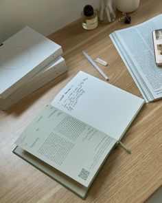 an open book sitting on top of a wooden table next to a cell phone and pen