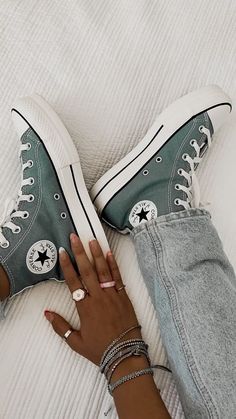 a woman's hand resting on top of her green converse - style sneakers, which are stacked with bracelets and rings