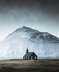 a small church in front of a mountain with snow on the top and grass below