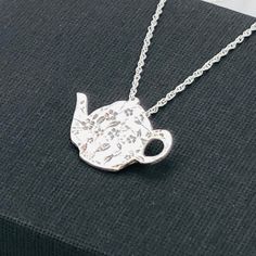 a silver teapot necklace on a black box