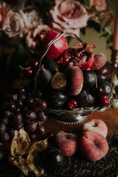 a bowl filled with fruit sitting on top of a table next to flowers and candles