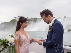 a man and woman standing next to each other in front of a waterfall holding hands