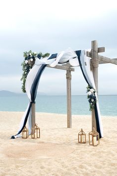 an outdoor wedding setup on the beach with blue and white draping, lanterns and flowers