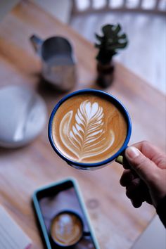 a person holding a cup of latte with a leaf design on the foam in front of them